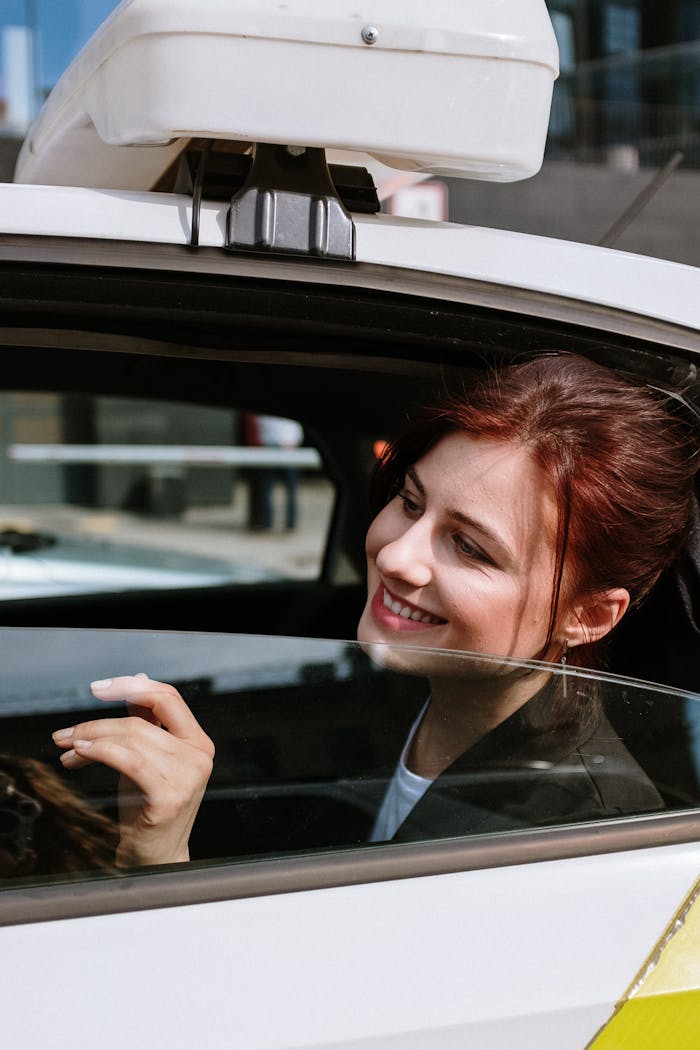 A cheerful woman smiles from the backseat of a moving taxi, city street view.